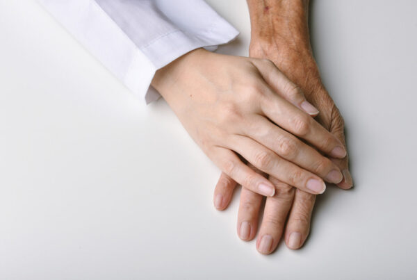 The hand of an adult female rests on top of her elderly mother's hand