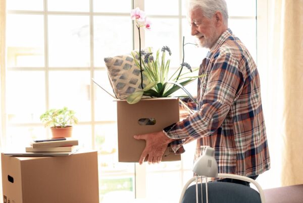 An older gentleman carries a moving box