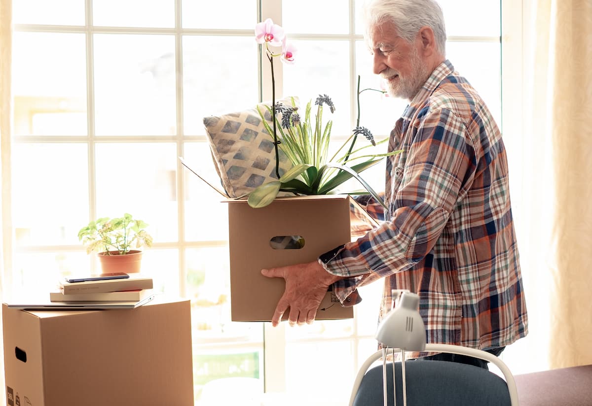 An older gentleman carries a moving box